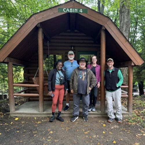 A group of male and female hikers in front of a cabin labelled "cabin 4."